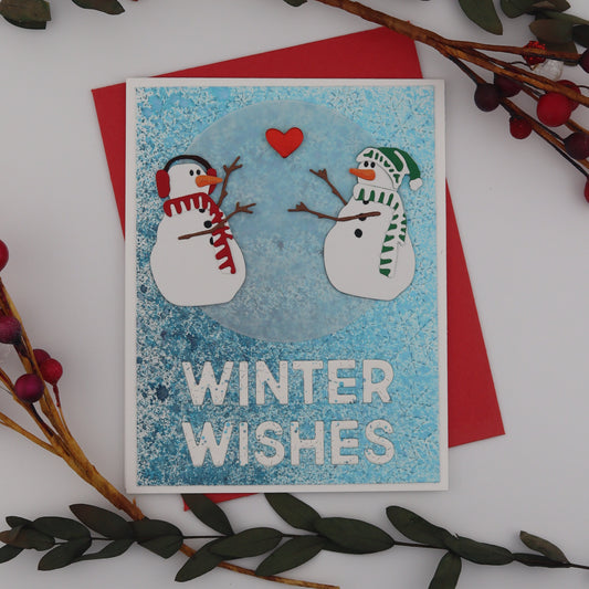 Card with snowmen and 'Winter Wishes' text, surrounded by decorative branches on a white background