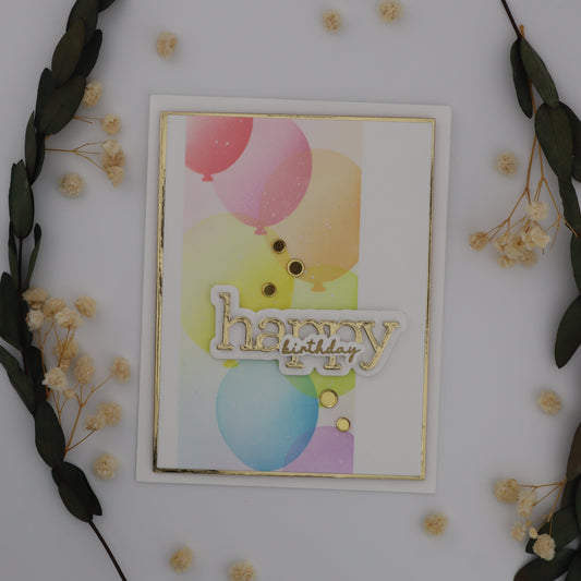 Decorative card with colorful balloons and 'Happy' text, surrounded by greenery and small flowers on a white background.
