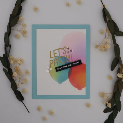 Colorful card with 'Let's Party!' text on a white surface with decorative elements.
