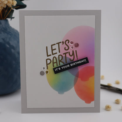 Colorful birthday card with 'Let's Party' text on a white background with decorative elements.