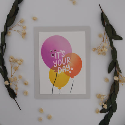 Decorative wall art with balloons and 'It's Your Day' text, surrounded by flowers and leaves.