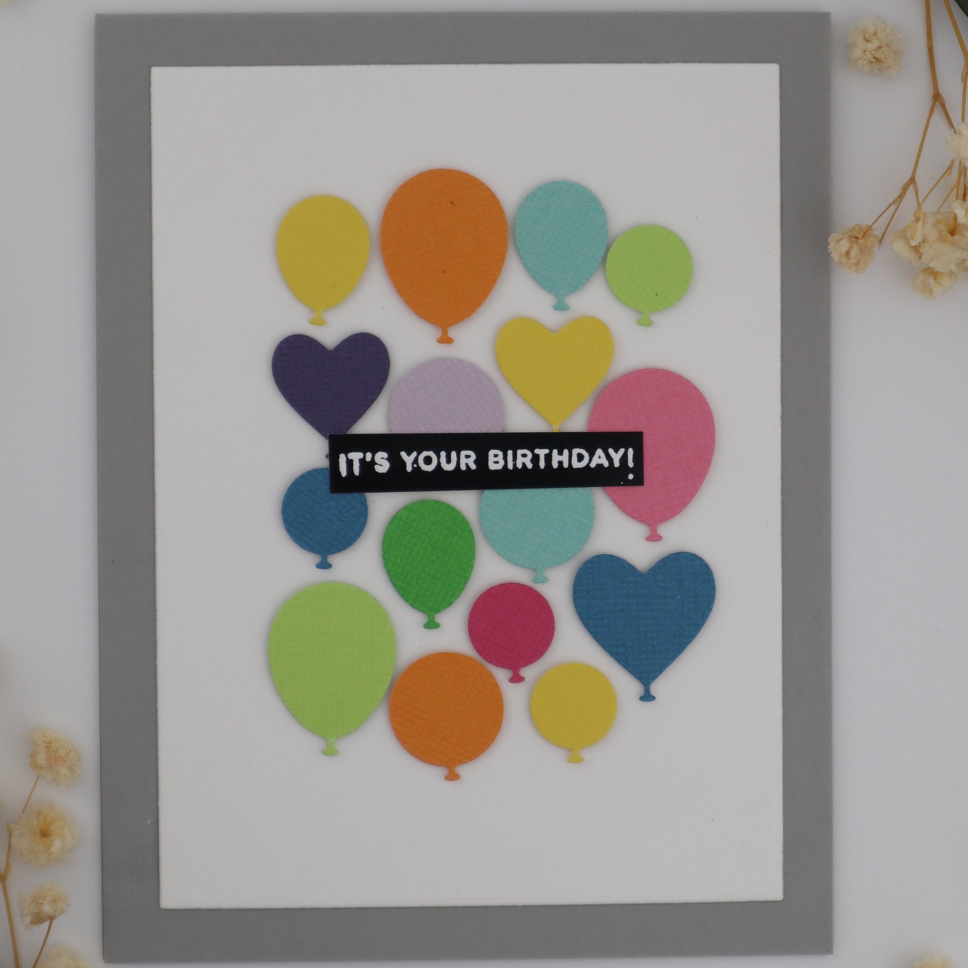 Framed card with colorful balloons and 'It's Your Birthday!' text on a white background with flowers.