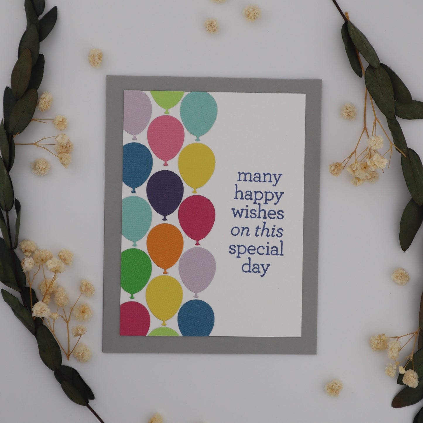 Framed card with colorful balloons and text on a white wall with decorative elements.