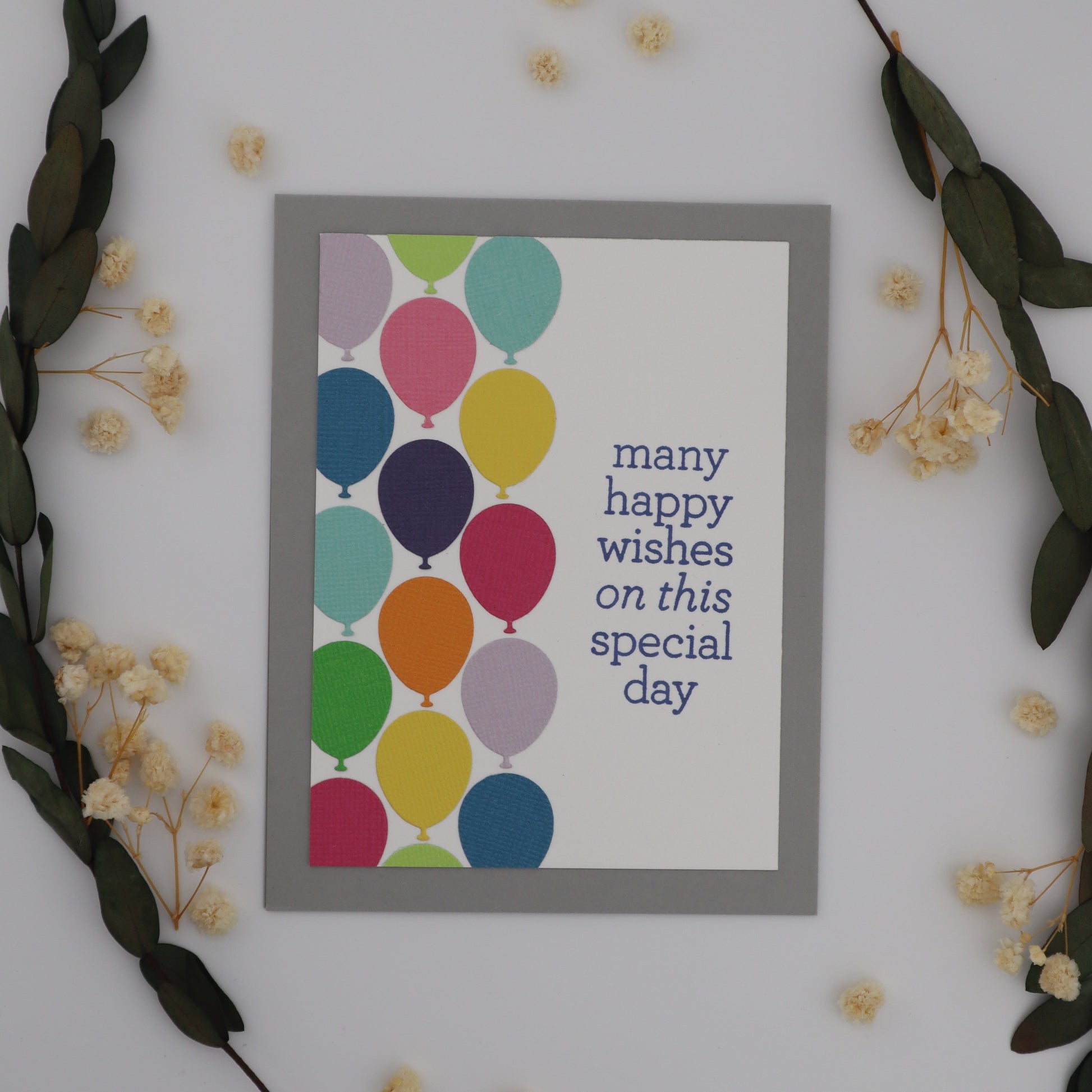 Framed card with colorful balloons and text on a white wall with decorative elements.