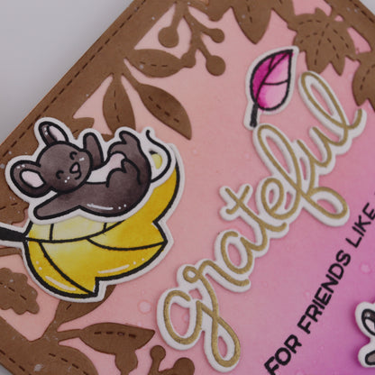 Card with a cartoon mouse on a banana, surrounded by leaves and flowers, with the word 'grateful' printed on it.