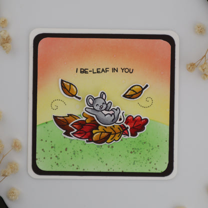 Card with a cartoon bear surrounded by leaves on a gradient background with flowers around.