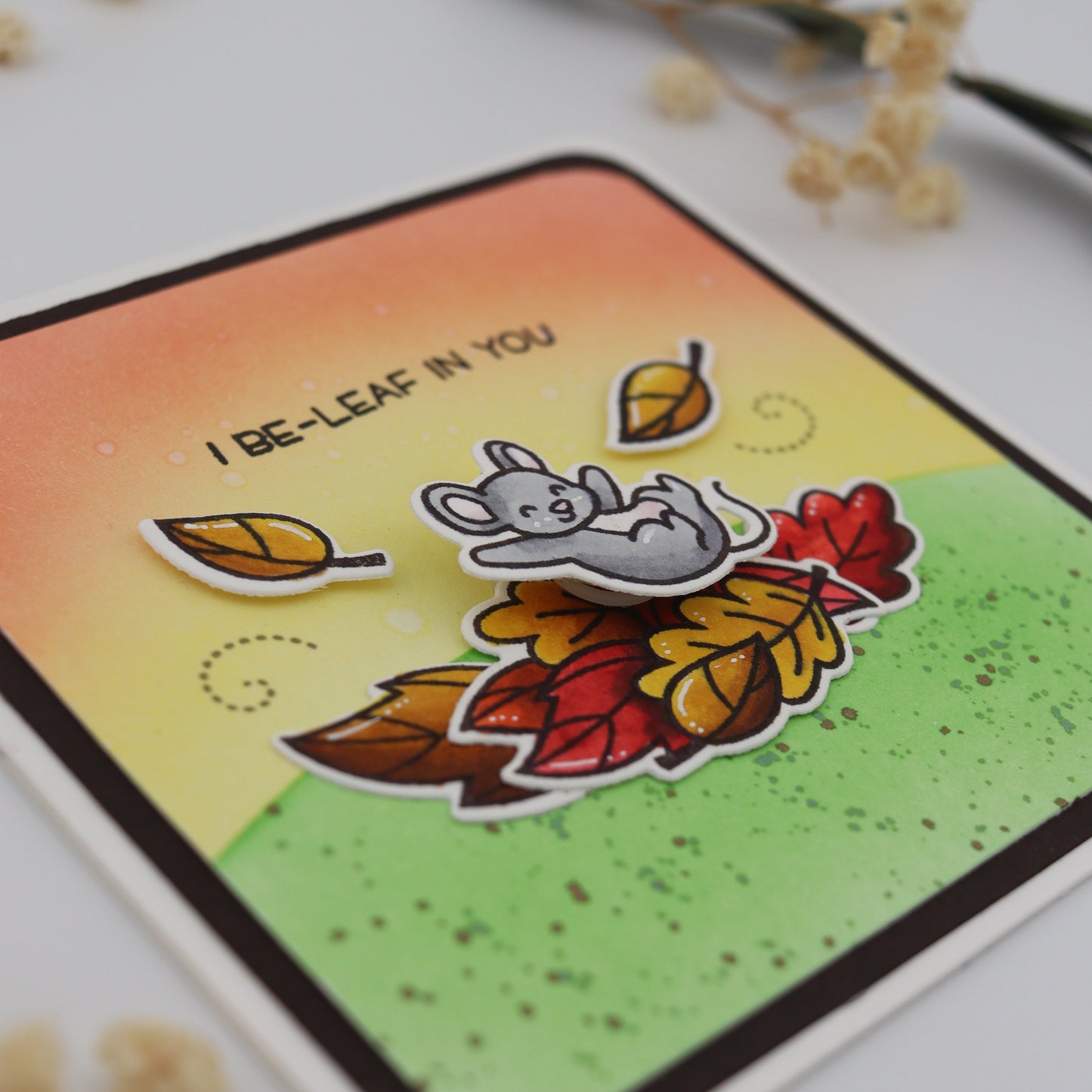 Card with autumn-themed design featuring leaves and a mouse, on a textured surface.