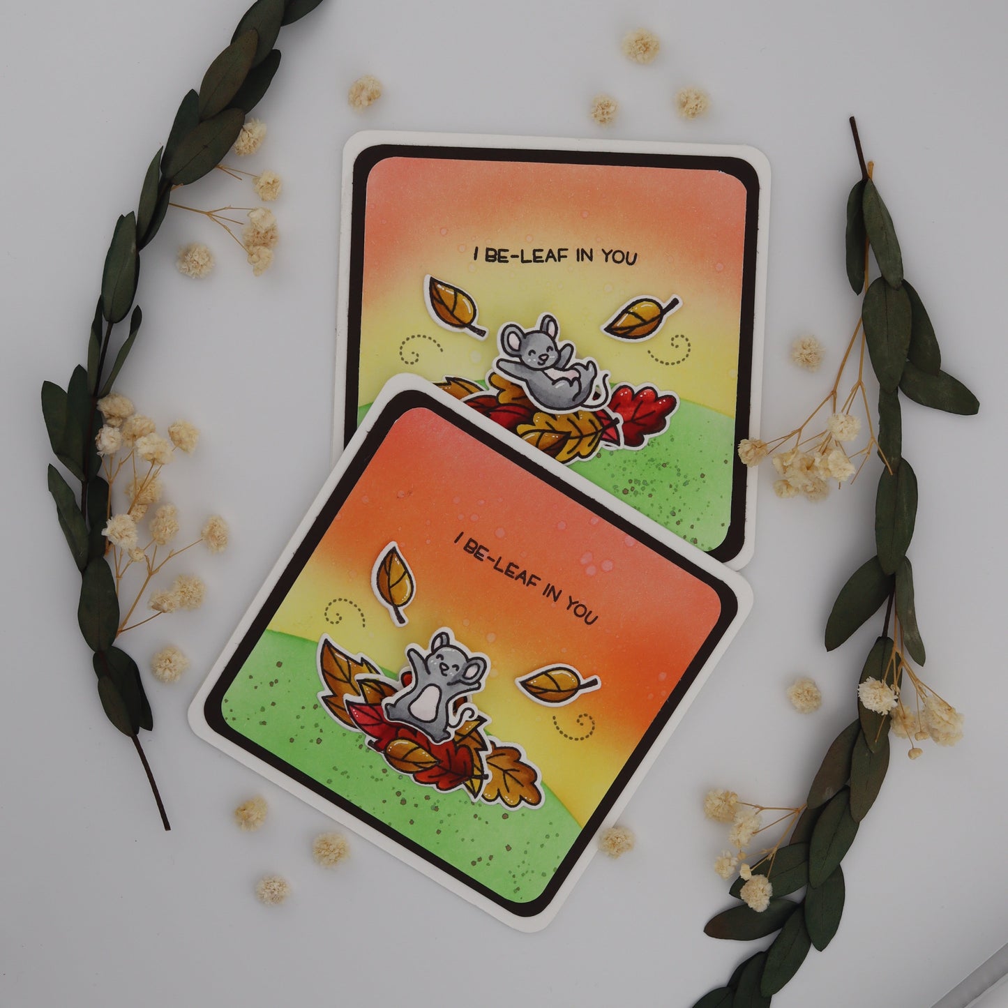 Two identical cards with a cat and leaf design on a white background with decorative elements.
