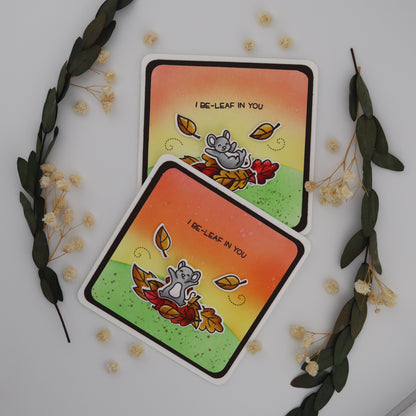 Two identical cards with a cat and leaf design on a white background with decorative elements.