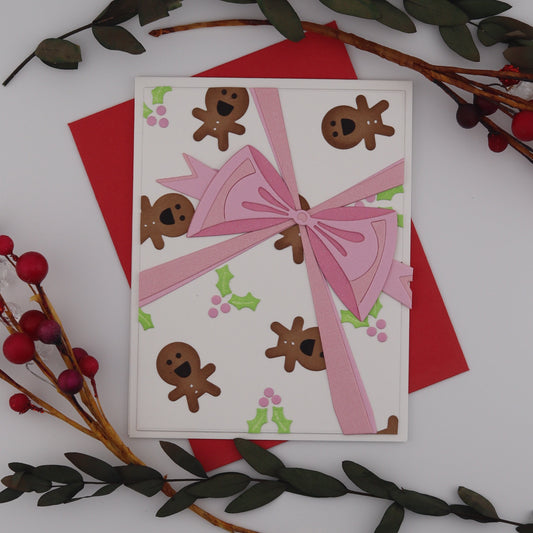 Card with pink bow and gingerbread men design on a white background with decorative branches.
