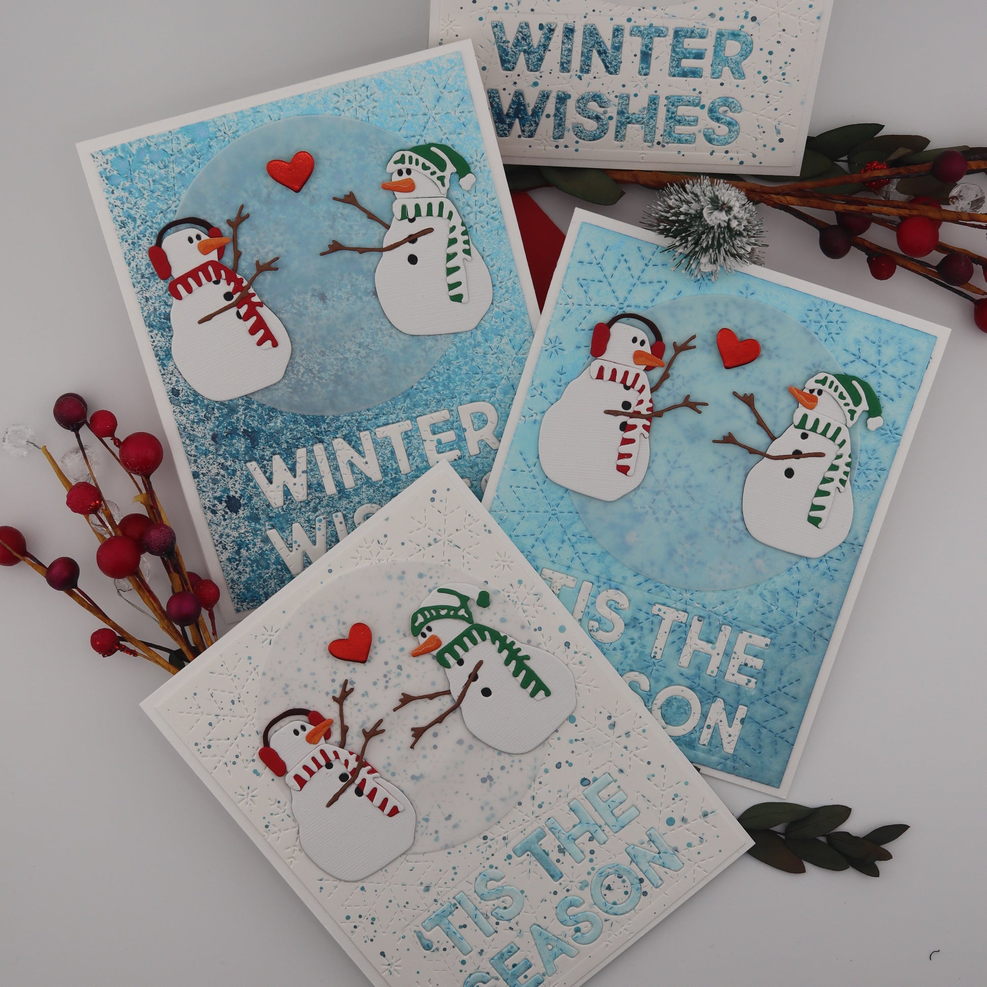 Set of four winter-themed greeting cards with snowmen and text on a white surface.