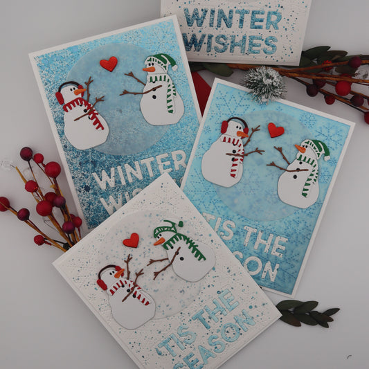 Set of four winter-themed greeting cards with snowmen and text on a white surface.