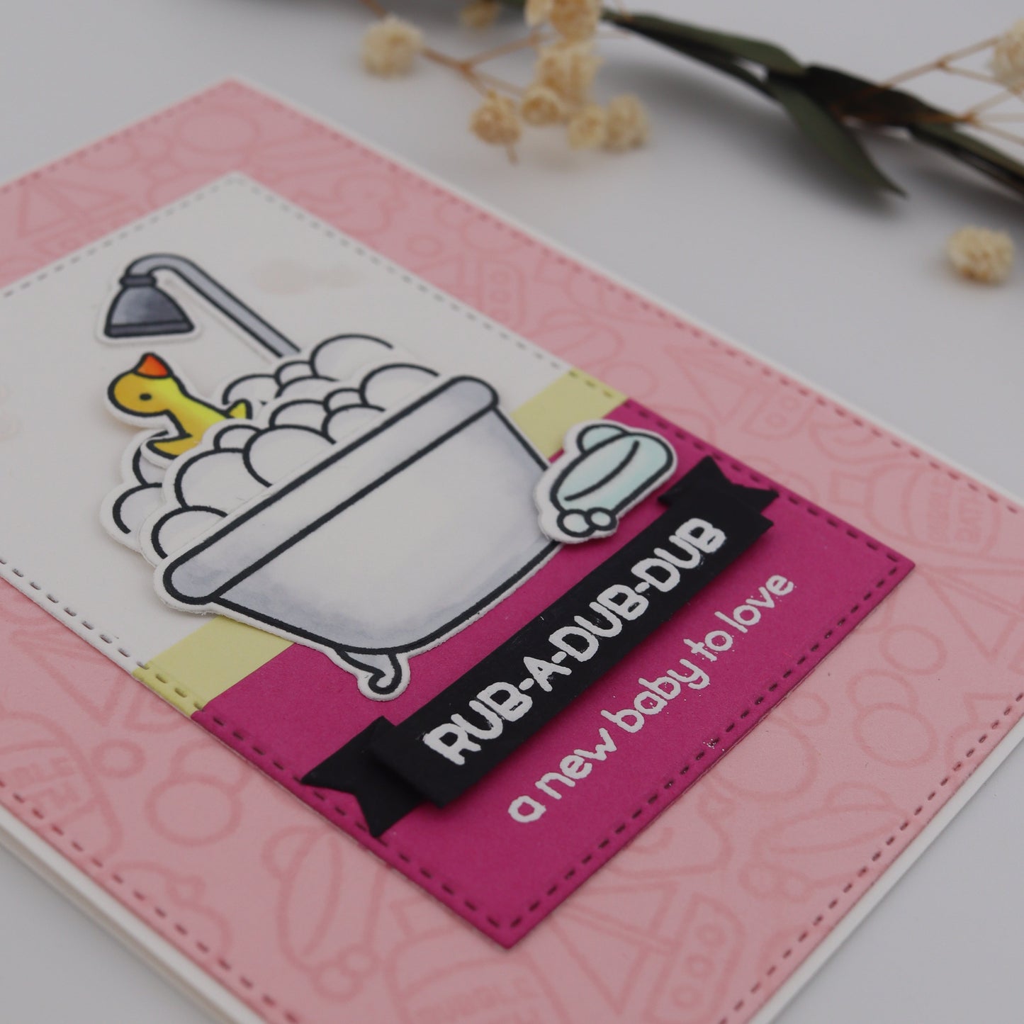 Pink card with baby-themed design and text 'Rub a dub dub, a new baby to love' on a light background.
