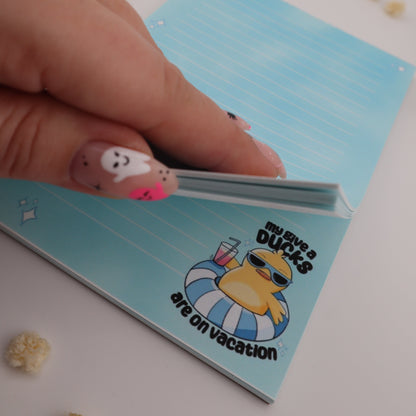 Hand holding a small object with a blue notepad featuring a cartoon character in the background.