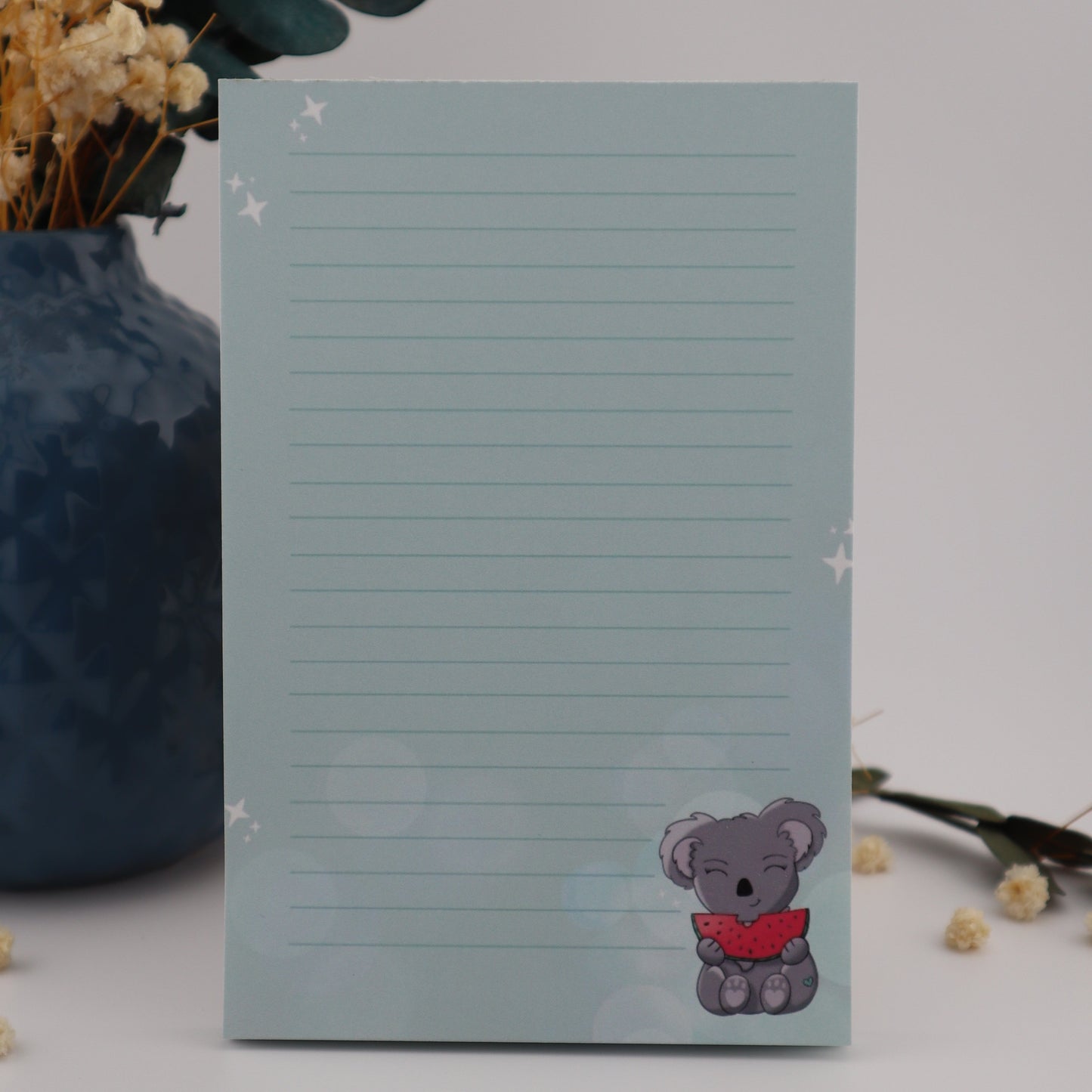 Notepad with a teddy bear design on a light gray background with decorative elements.