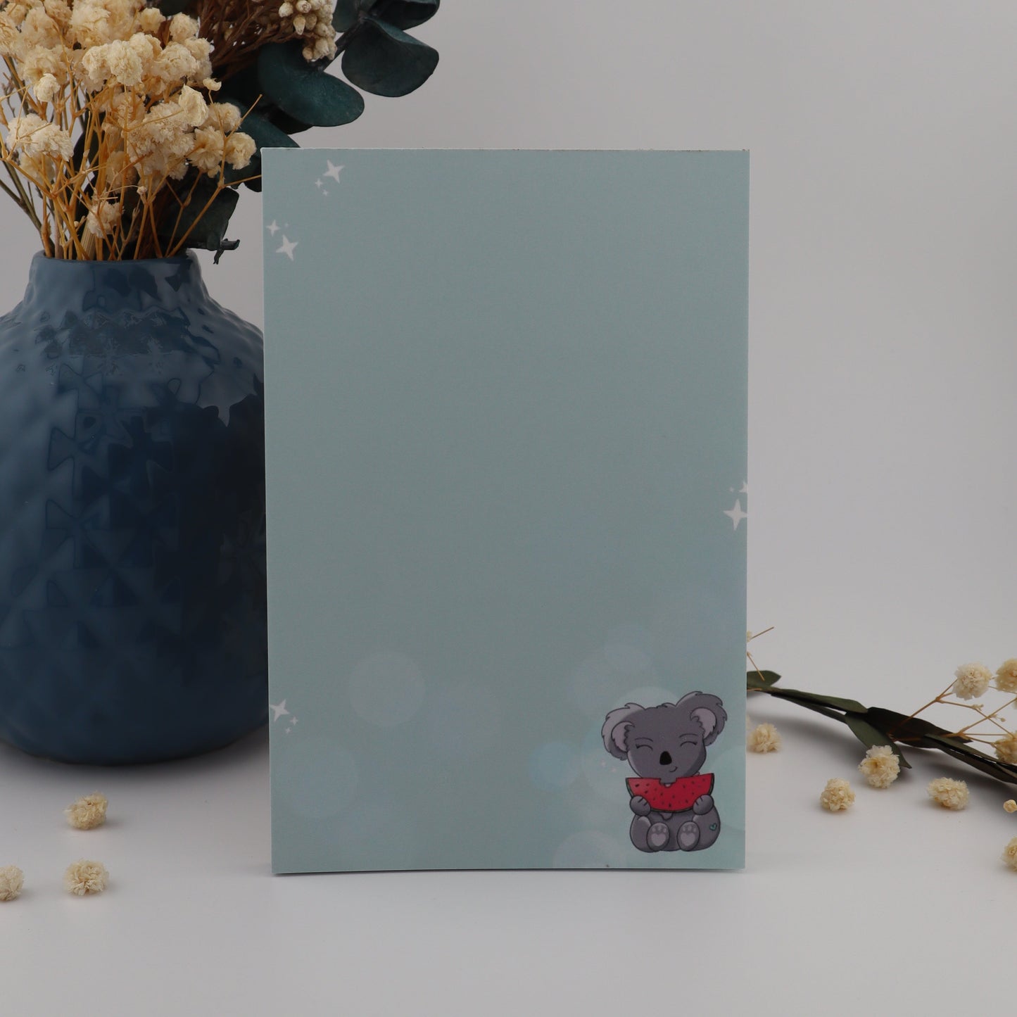 Decorative setup with a vase, flowers, and a card featuring a bear design on a light gray background.