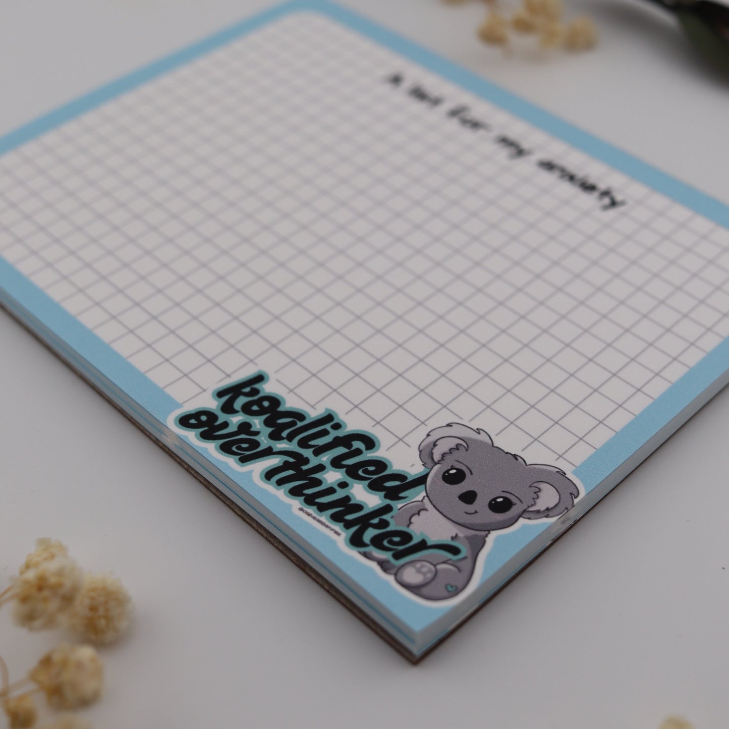 Notebook with a cartoon mouse sticker on a white surface with dried flowers.