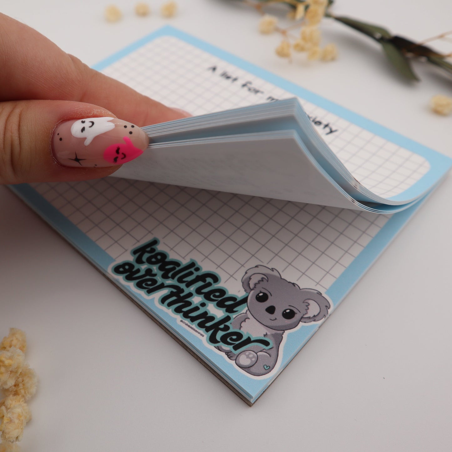 Small notebook with a teddy bear design and text held by a hand on a light surface.