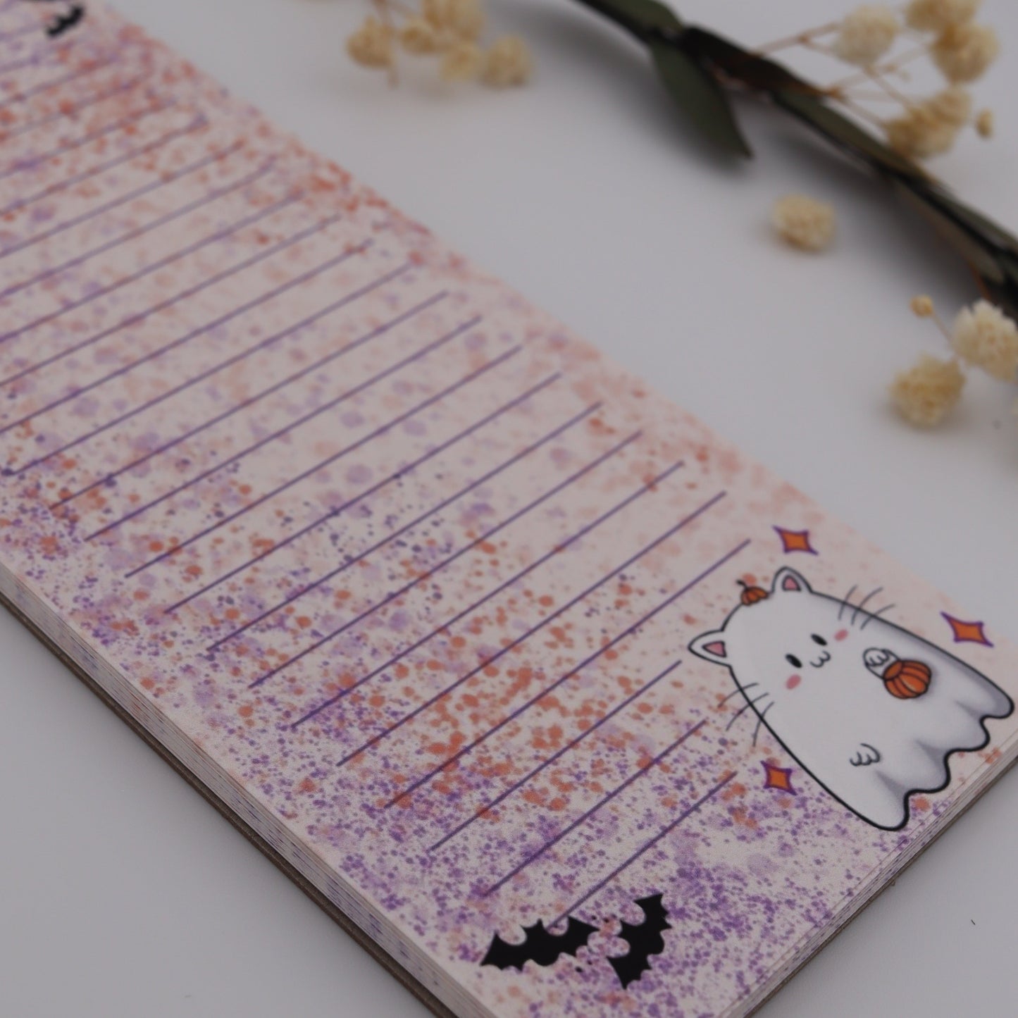 Notebook with Halloween-themed design on a white surface with dried flowers.