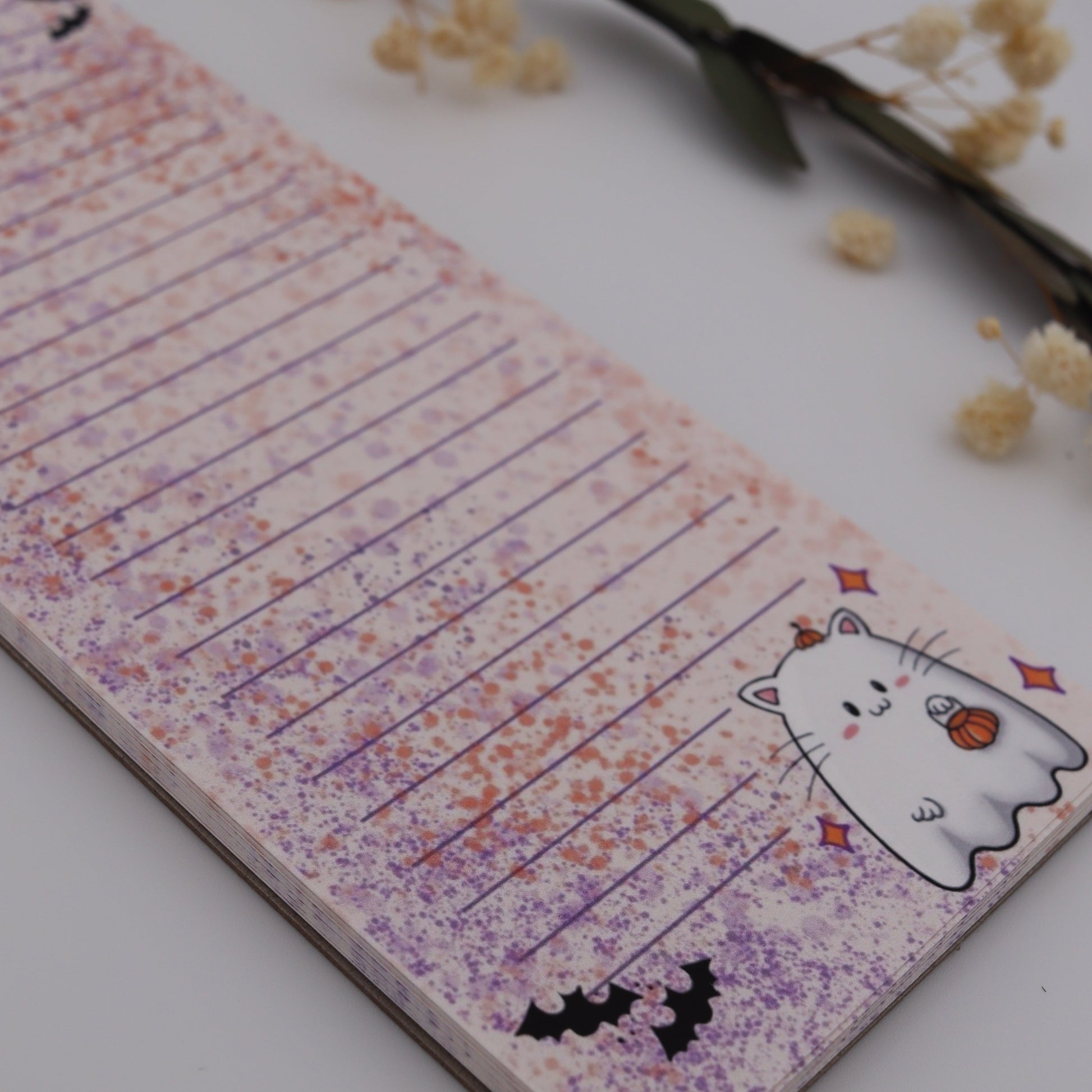 Notebook with Halloween-themed design on a white surface with dried flowers.