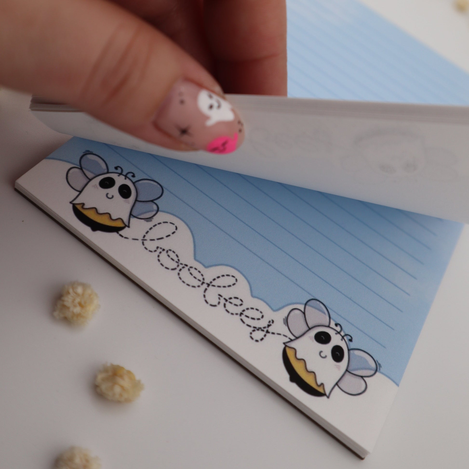 Hand holding a small notebook with cartoon character design on a white surface.