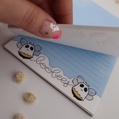 Hand holding a small notebook with cartoon character design on a white surface.